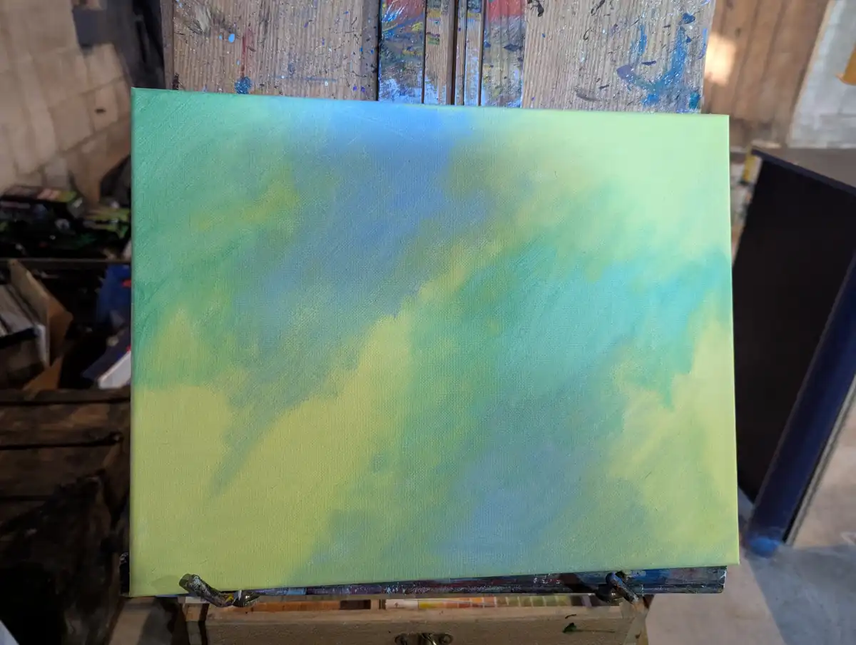 A canvas on an easel displays a blurry, abstract blend of green, yellow, and blue paint, resembling a sunset. The background…