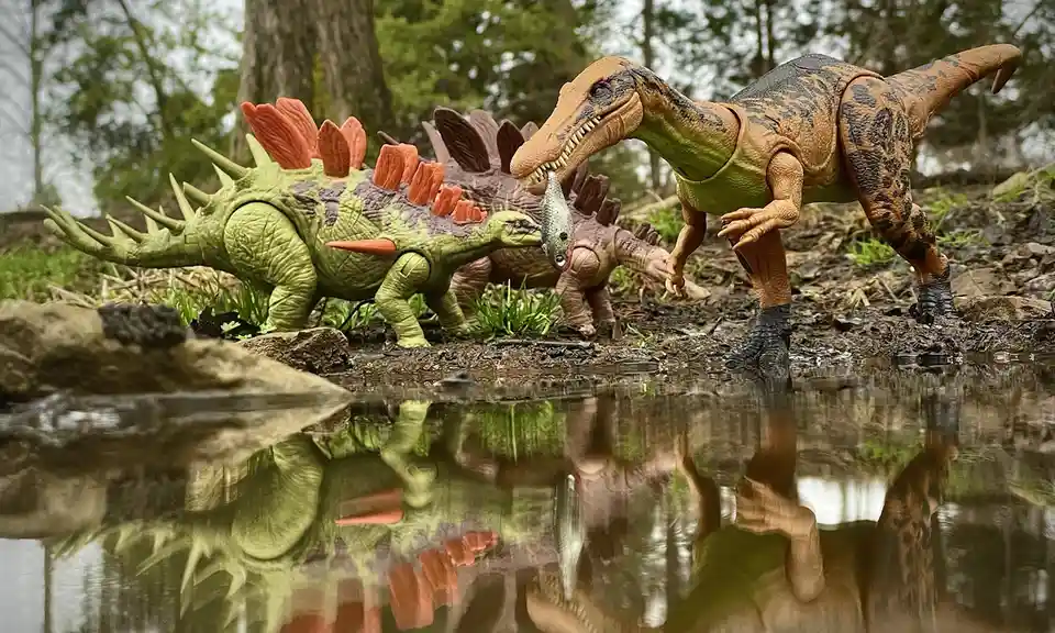 A photo of toy dinosaurs staged near a pond, where a predatory dinosaur holds a fishing lure in its mouth, while a…