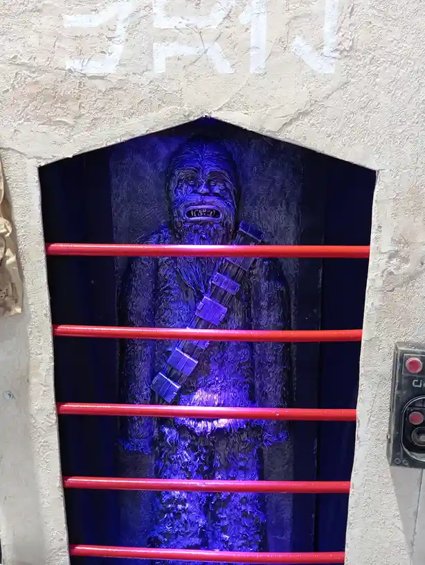 A statue of the Star Wars character Chewbacca is illuminated in blue light and viewed through red horizontal bars, with the…