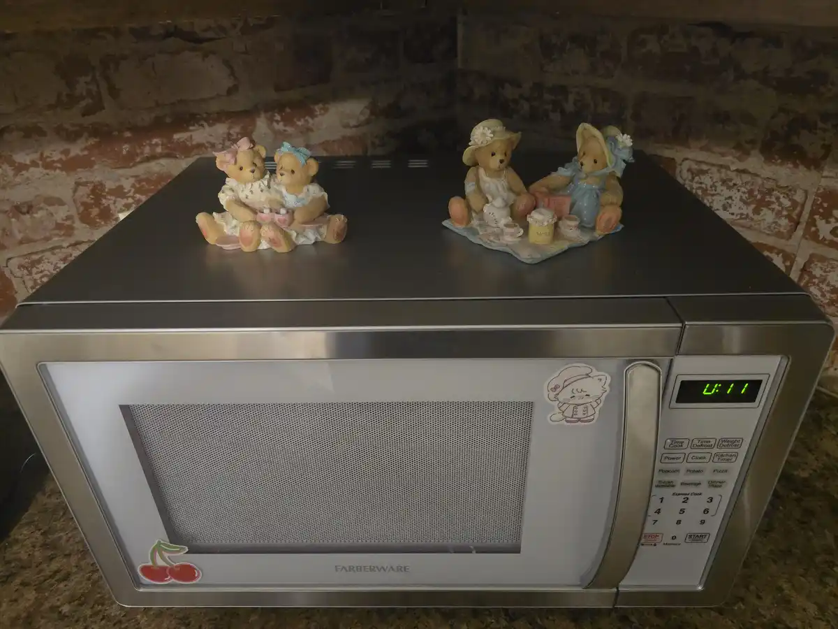 A stainless steel Farberware microwave sits on a granite countertop against a stone wall, displaying a digital clock reading…