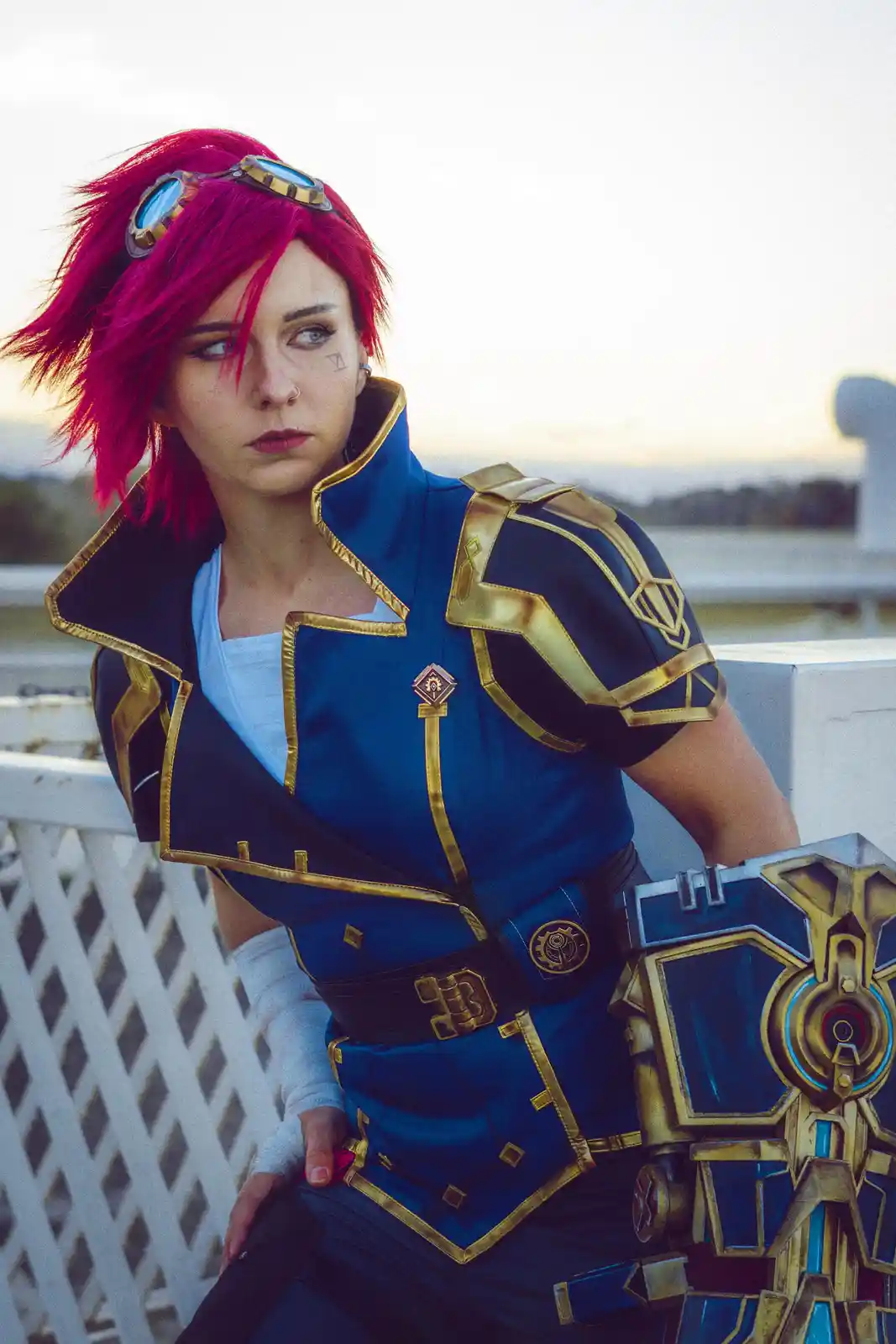 A person in a detailed cosplay of the character Jinx from League of Legends, featuring bright pink hair, goggles on their…