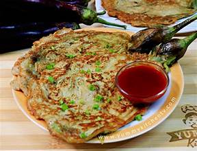 A close-up photo of a golden-brown, round, savory pancake or omelet garnished with chopped green onions, served on a white…