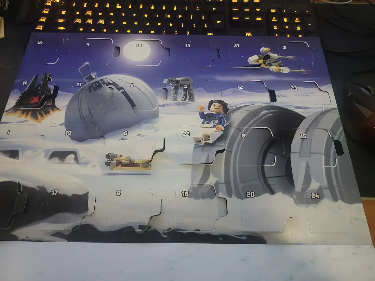 A Lego Star Wars Advent Calendar is shown with many numbered compartments open, revealing miniatures like a snowspeeder, an…