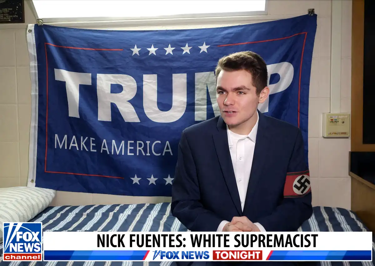 A young man in a suit sits on a bed in front of a blue 'TRUMP MAKE AMERICA' banner. He wears a red armband with a swastika…
