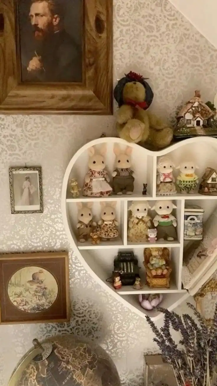A heart-shaped white shelf filled with miniature Sylvanian Families dolls and collectibles, mounted on a wall with patterned…