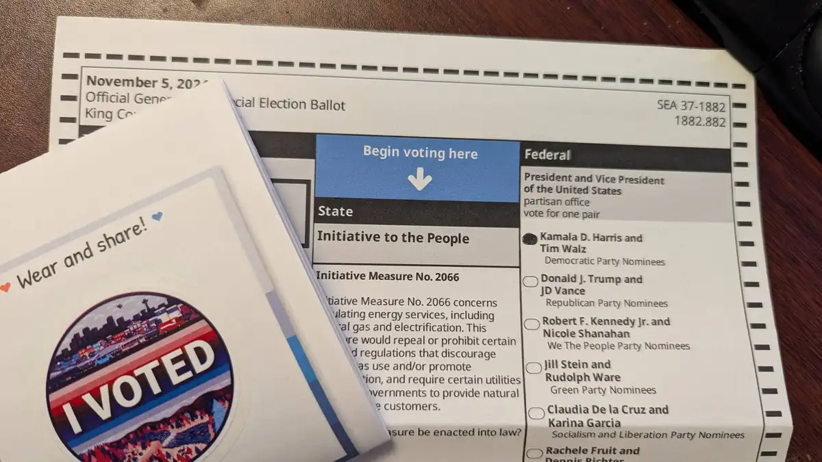A close-up photo shows a 2024 King County official general election ballot with a blue 'Begin voting here' arrow pointing…