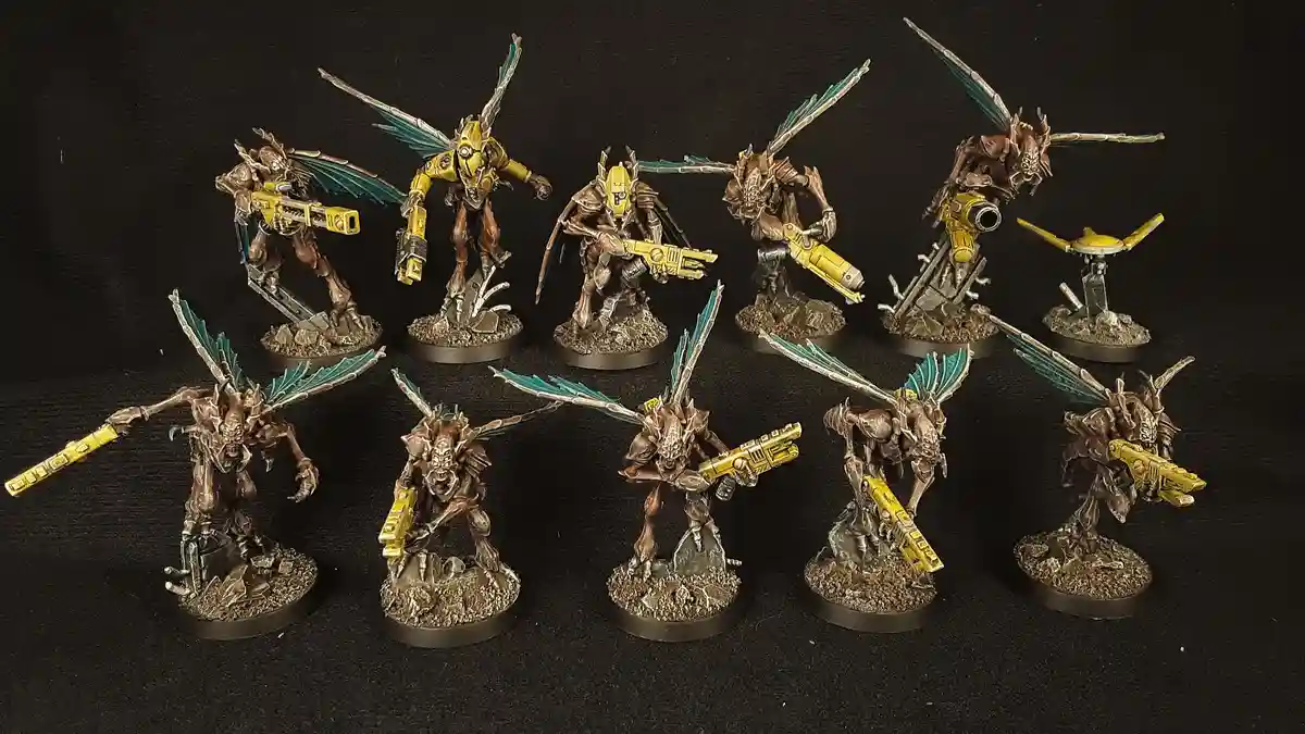 A collection of nine intricately painted, biomechanical insectoid miniatures with teal wings and yellow weaponry, arranged…
