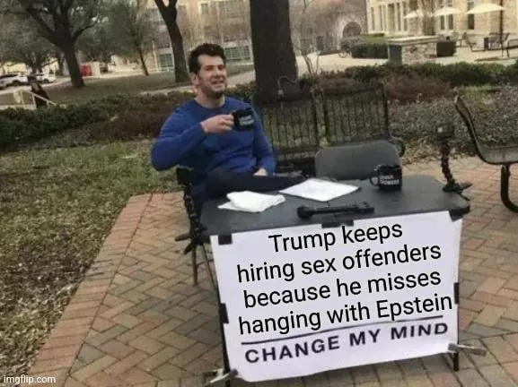 A man in a blue shirt sits at a makeshift outdoor desk with a sign that reads 'Trump keeps hiring sex offenders because he…