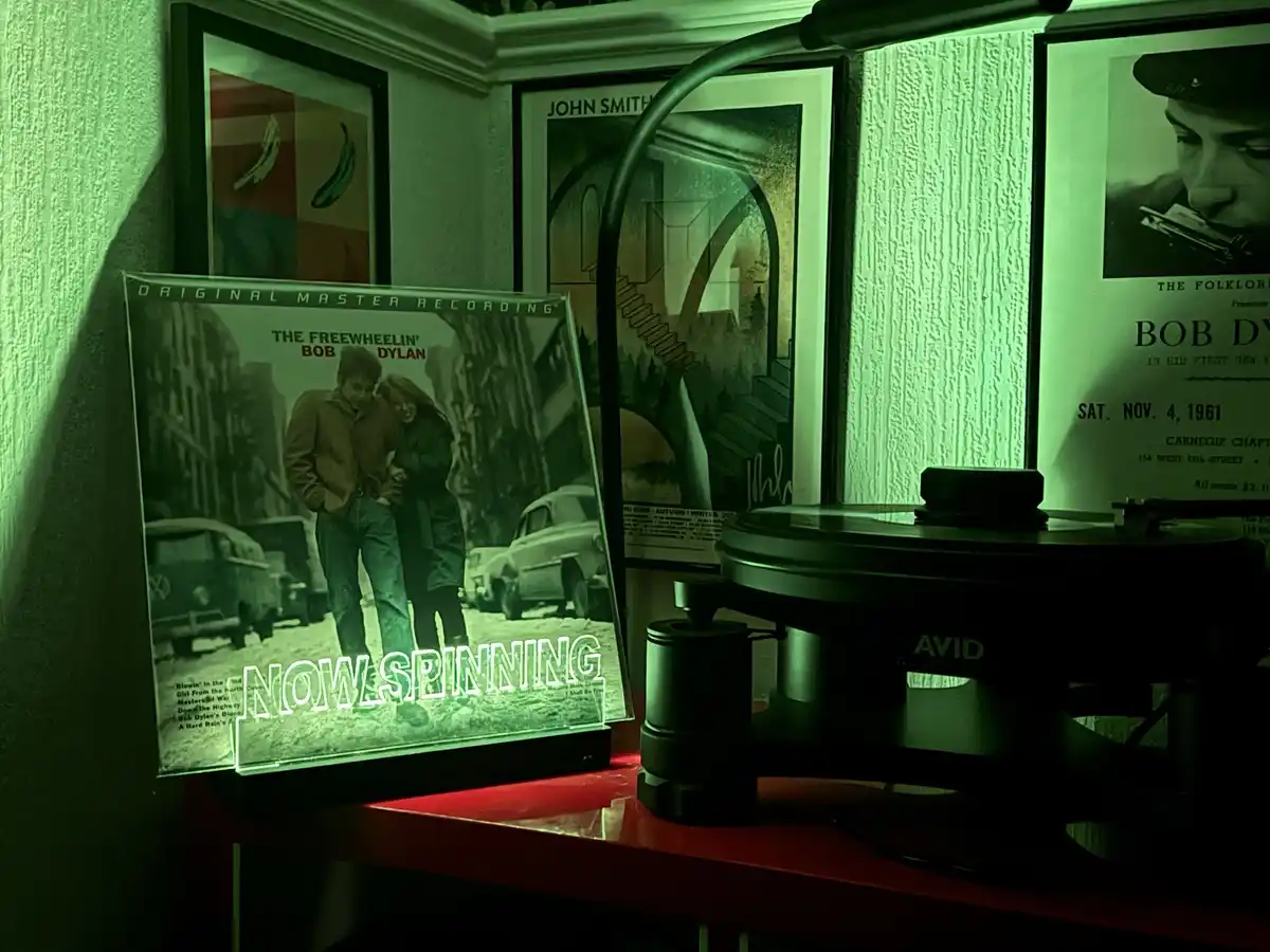 A dimly lit room bathed in green light features a record player on a red shelf, next to a glowing illuminated display of Bob…