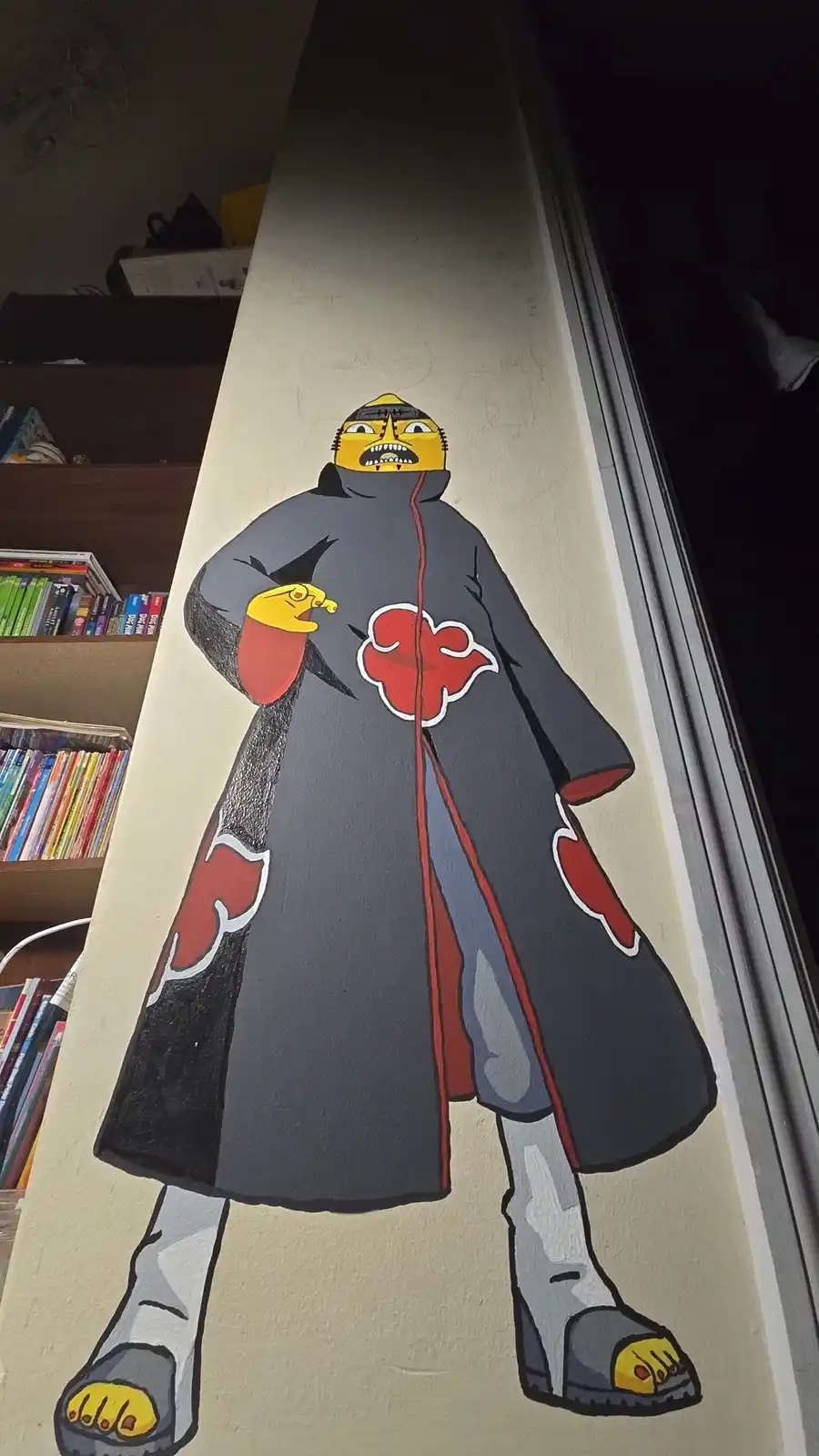 A hand-painted mural on a wall depicts a character in a grey Akatsuki cloak with red cloud insignia, but the face is…