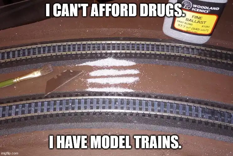 A close-up photo of a model train layout with curved tracks on brown baseboard. A small pile of white powder, resembling…