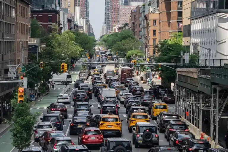 A high-angle photo of a heavily congested city street filled with cars, including yellow taxis, stretching into the distance…