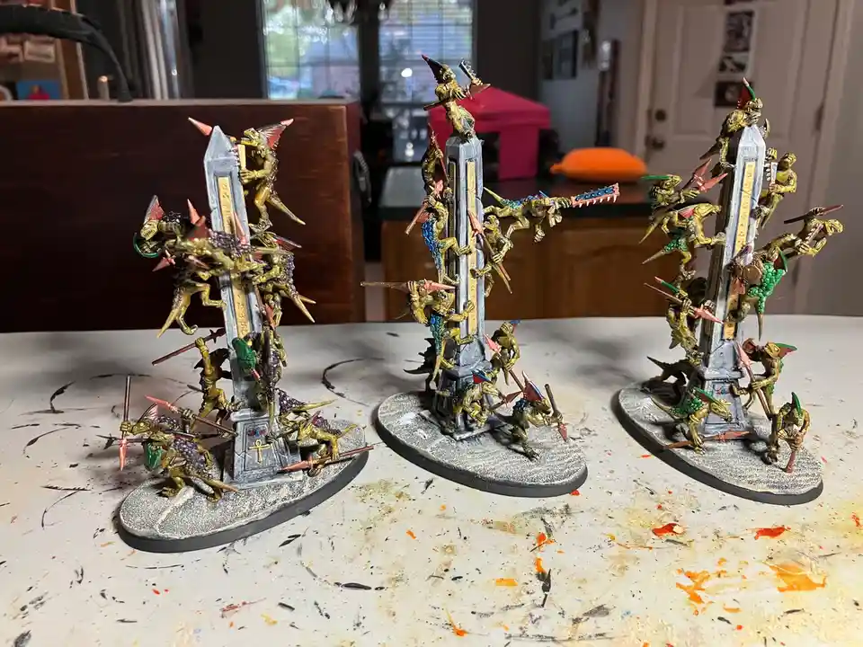 Three intricately painted miniature warlord figures, each mounted on a tall grey obelisk base and surrounded by smaller…