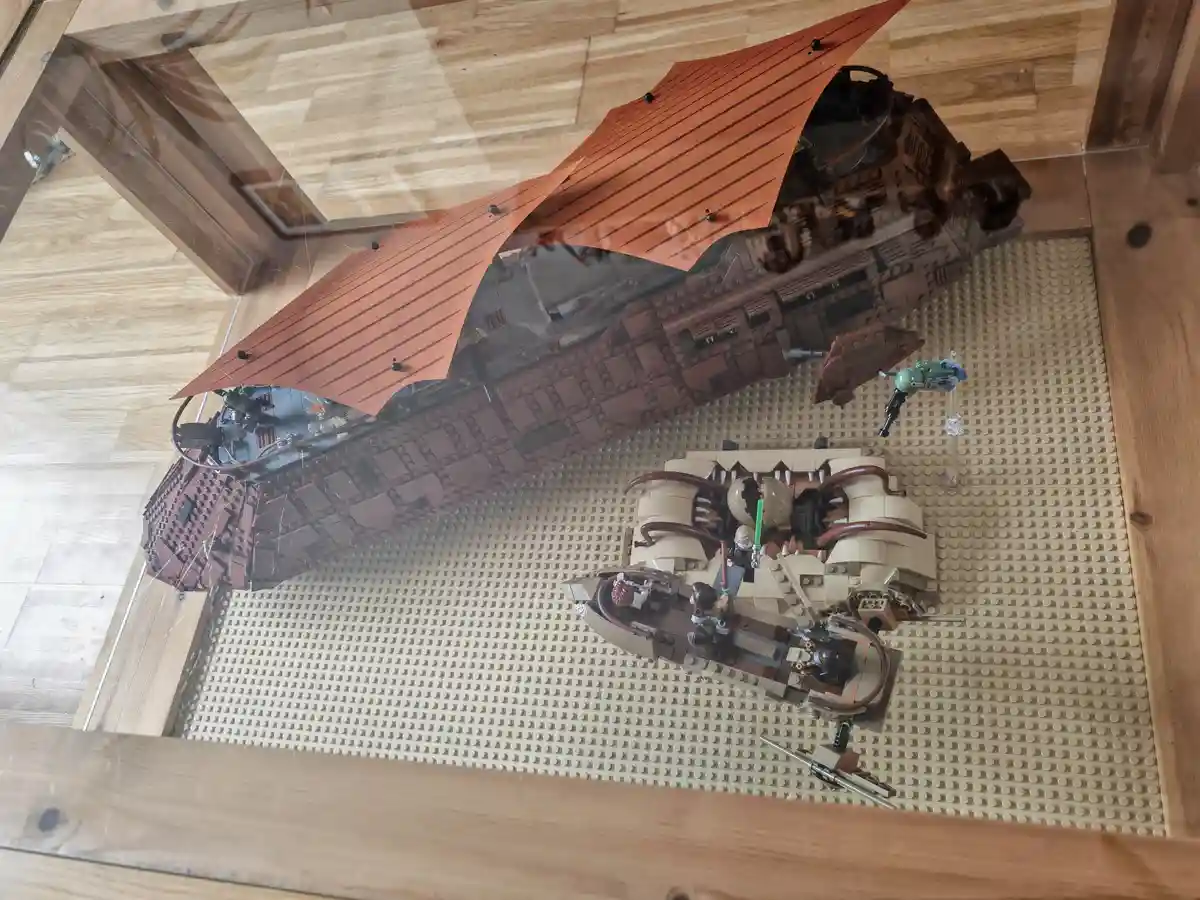 An overhead view shows a large, detailed LEGO Star Wars model of a spaceship with orange sails, displayed on a beige LEGO…