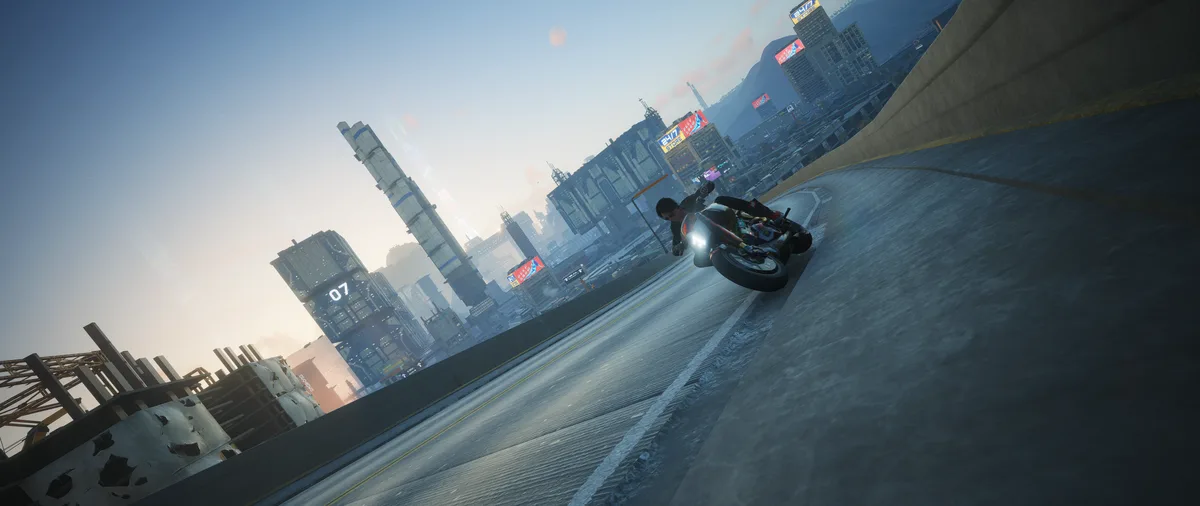 A video game screenshot shows a motorcycle rider leaning into a sharp turn on a highway overpass, with a sprawling…