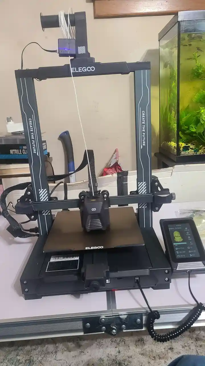 A black Elegoo 3D printer with 'CREATE THE FUTURE' printed vertically on its frame is actively printing a small green…