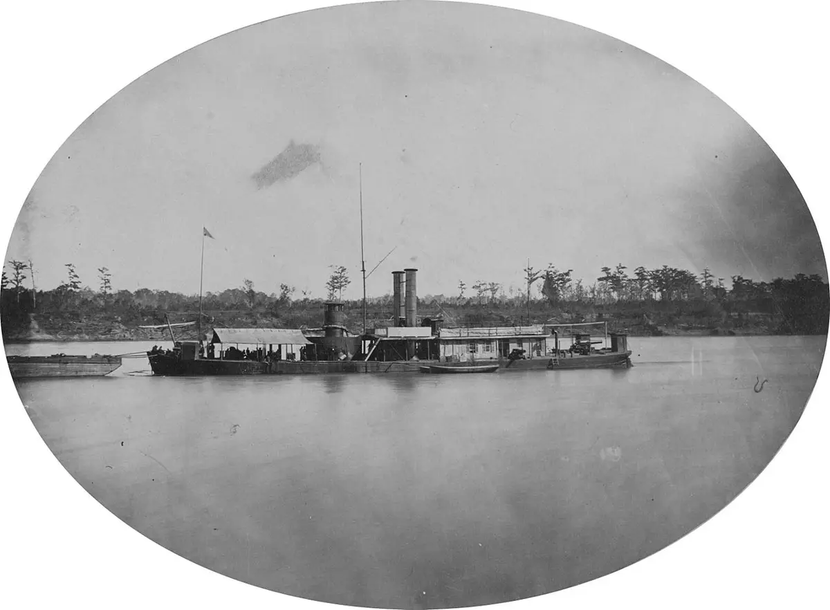 A vintage black-and-white photograph shows a steamboat on a river, with people visible on deck and trees lining the distant…