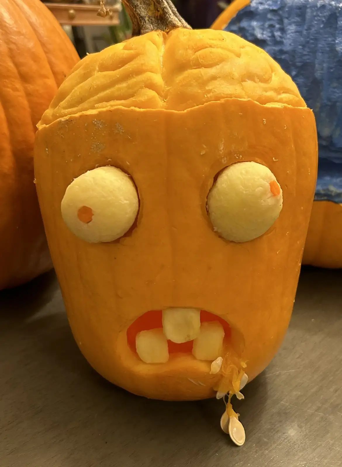 A close-up of a carved orange pumpkin with a comically exaggerated face, featuring large round white eyes with orange…