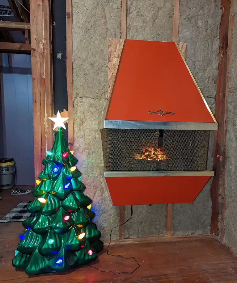 A small, green, plastic Christmas tree with colorful lights and a white star on top stands next to a modern, red-orange…