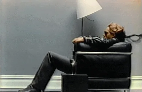 A man in a black leather chair is shown in six panels, progressively relaxing with his head back and legs up, while a black…
