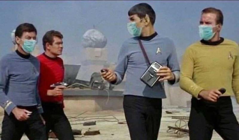 four men in star trek uniforms from the 1960s, wearing surgical masks and holding handheld devices, walk across a desolate…