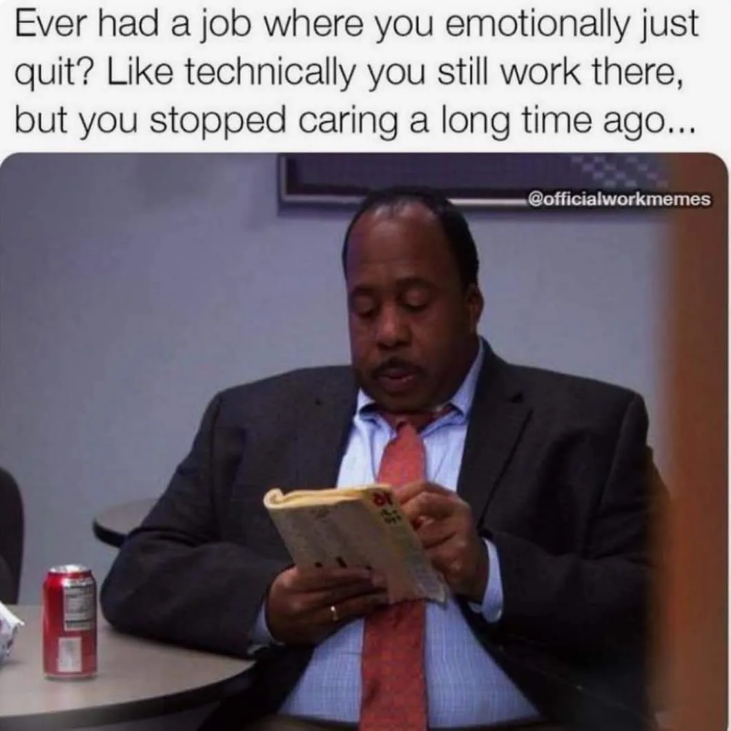 A man in a suit and tie sits at a desk, eyes closed, holding a newspaper as if reading it disinterestedly. A red soda can…