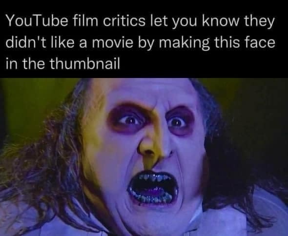 A close-up image of a person with pale makeup, wide eyes, and an open mouth showing teeth, conveying extreme horror or…