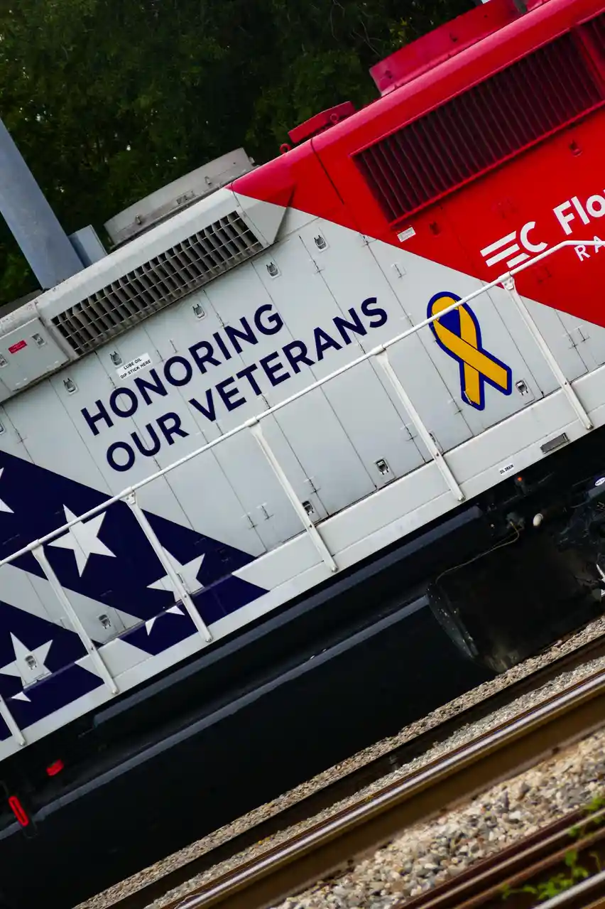 A red and white train engine with patriotic graphics, including stars and stripes and a yellow ribbon, displays the text…