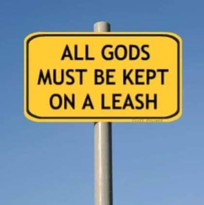 A yellow rectangular road sign with black text reads 'ALL GODS MUST BE KEPT ON A LEASH' against a clear blue sky. The sign…