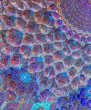 a close-up photograph of an ornate, geometrically patterned Islamic ceiling with intricate blue, purple, and gold tilework…