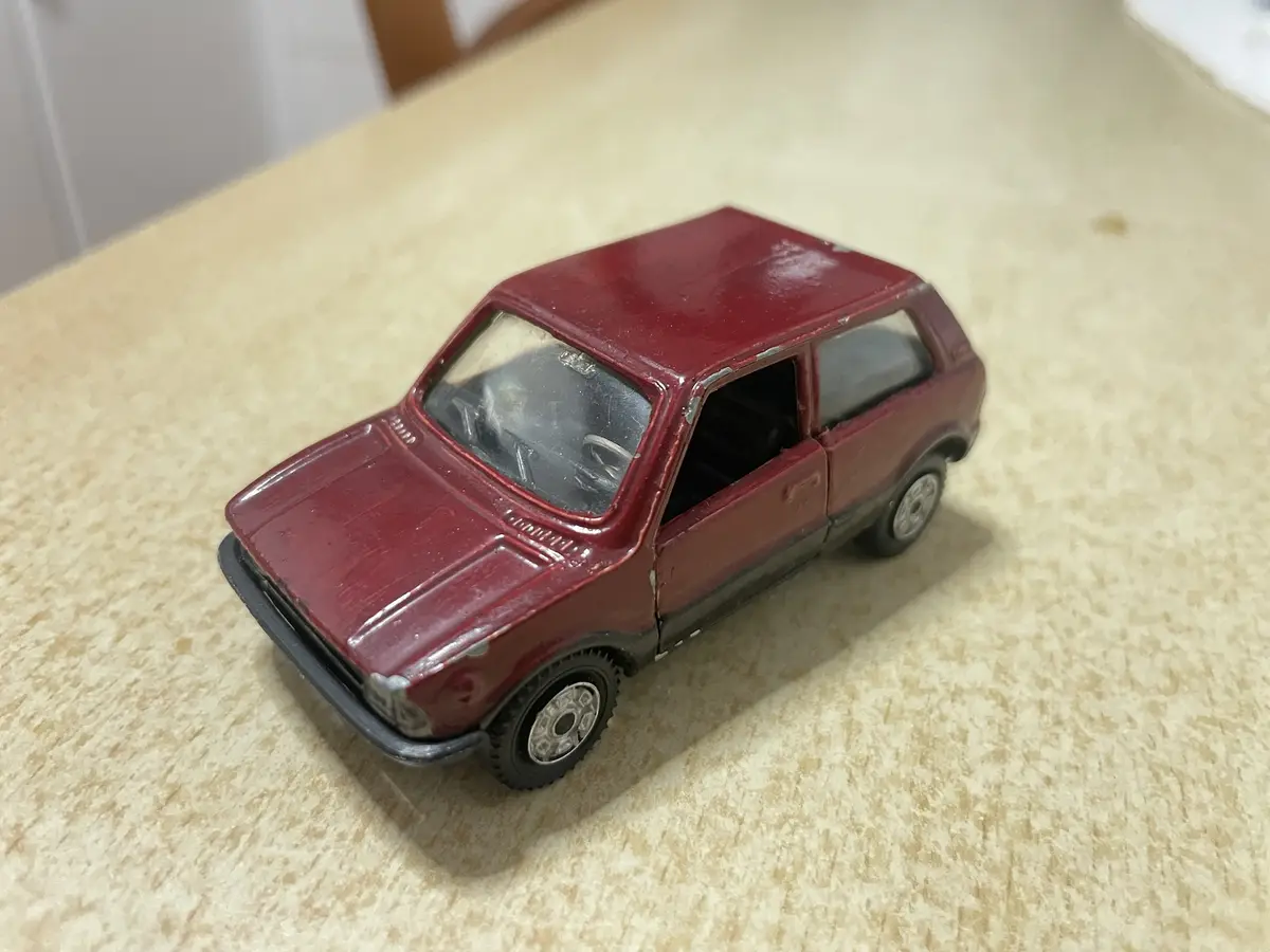 A small, red toy car with visible wear and tear sits on a speckled beige countertop. The car's door is open, revealing a…
