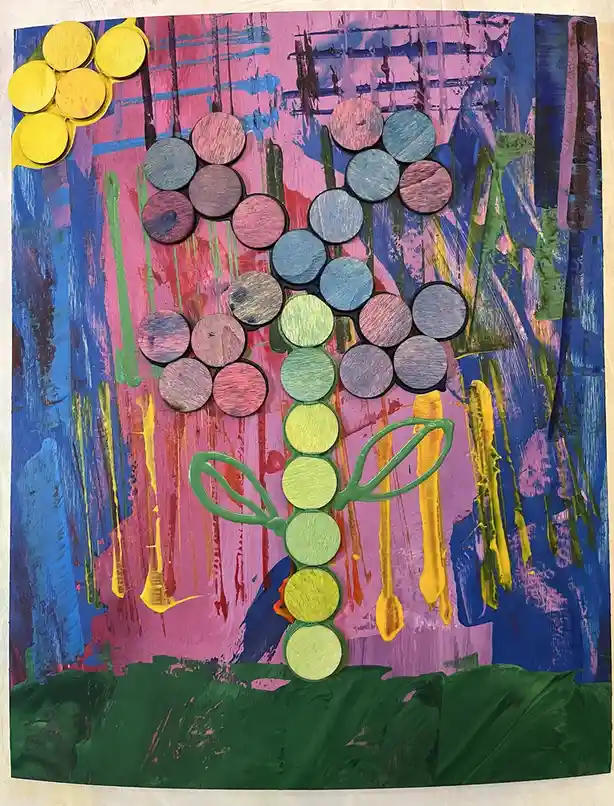 A colorful child's art project depicts a flower made of painted wooden circles arranged in petals and stem, set against a…