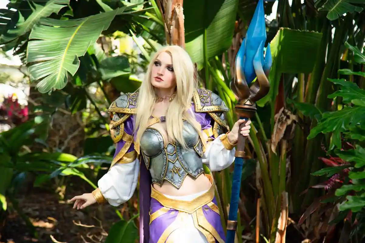 A person in a detailed cosplay of a fantasy character with blonde hair, silver and purple armor, and a blue-tipped staff…