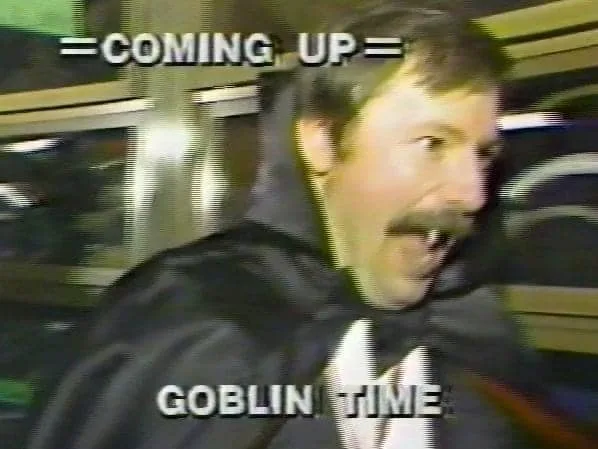 A grainy, VHS-style image shows a man with a mustache wearing a black cape and bowtie, looking excitedly to the side. Text…