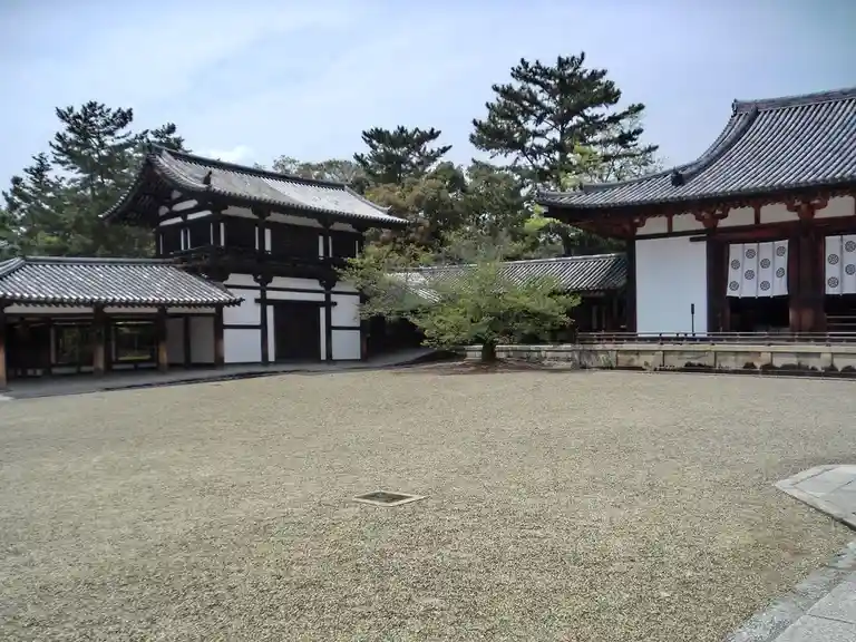A serene courtyard of traditional Japanese architecture with gravel ground, wooden buildings with tiled roofs, and trees…