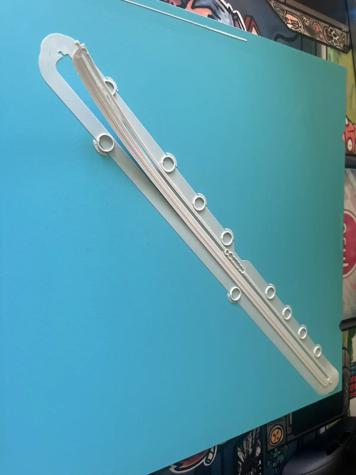 A 3D-printed white flute-like object with circular finger holes lies diagonally across a teal surface. The object has…