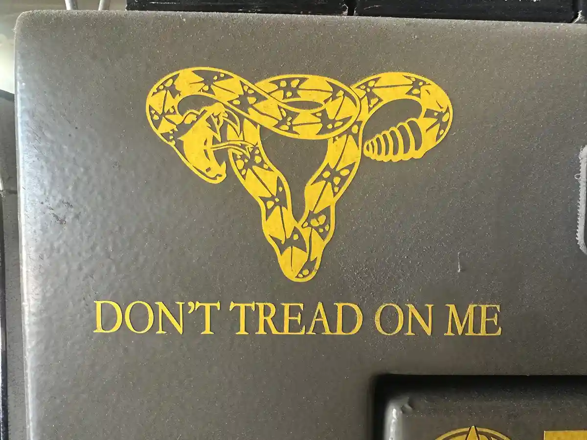 A close-up of a dark gray surface, likely a metal box or panel, featuring a yellow graphic of a coiled rattlesnake with its…
