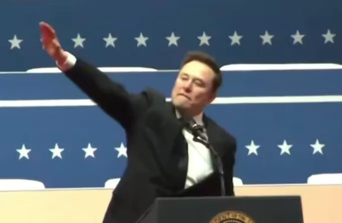 elon musk stands at a podium with a presidential seal, raising his right arm in a gesture resembling a presidential salute…