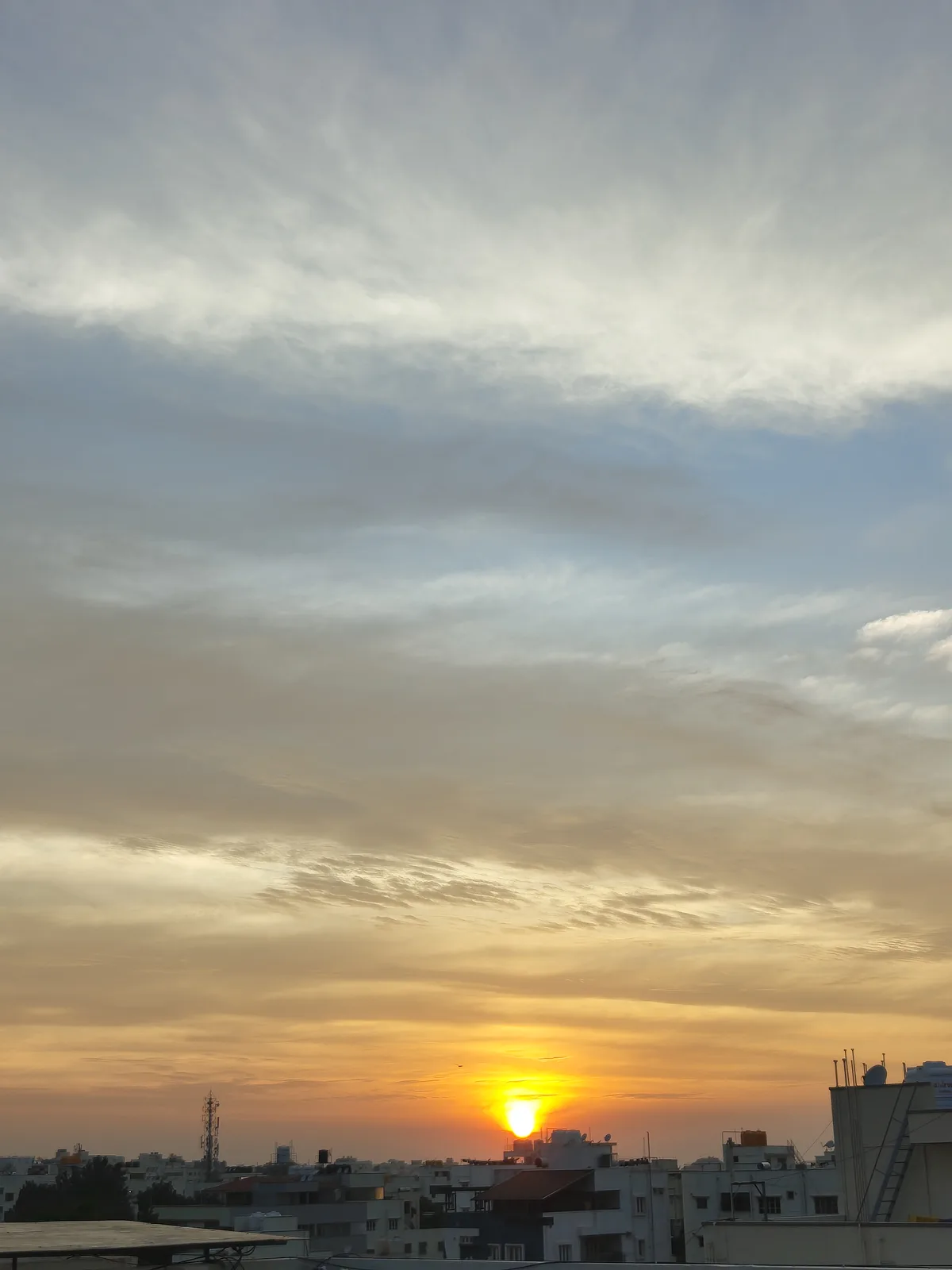 A photograph of a sunrise over a city skyline, with the sun low on the horizon casting golden light through wispy clouds…