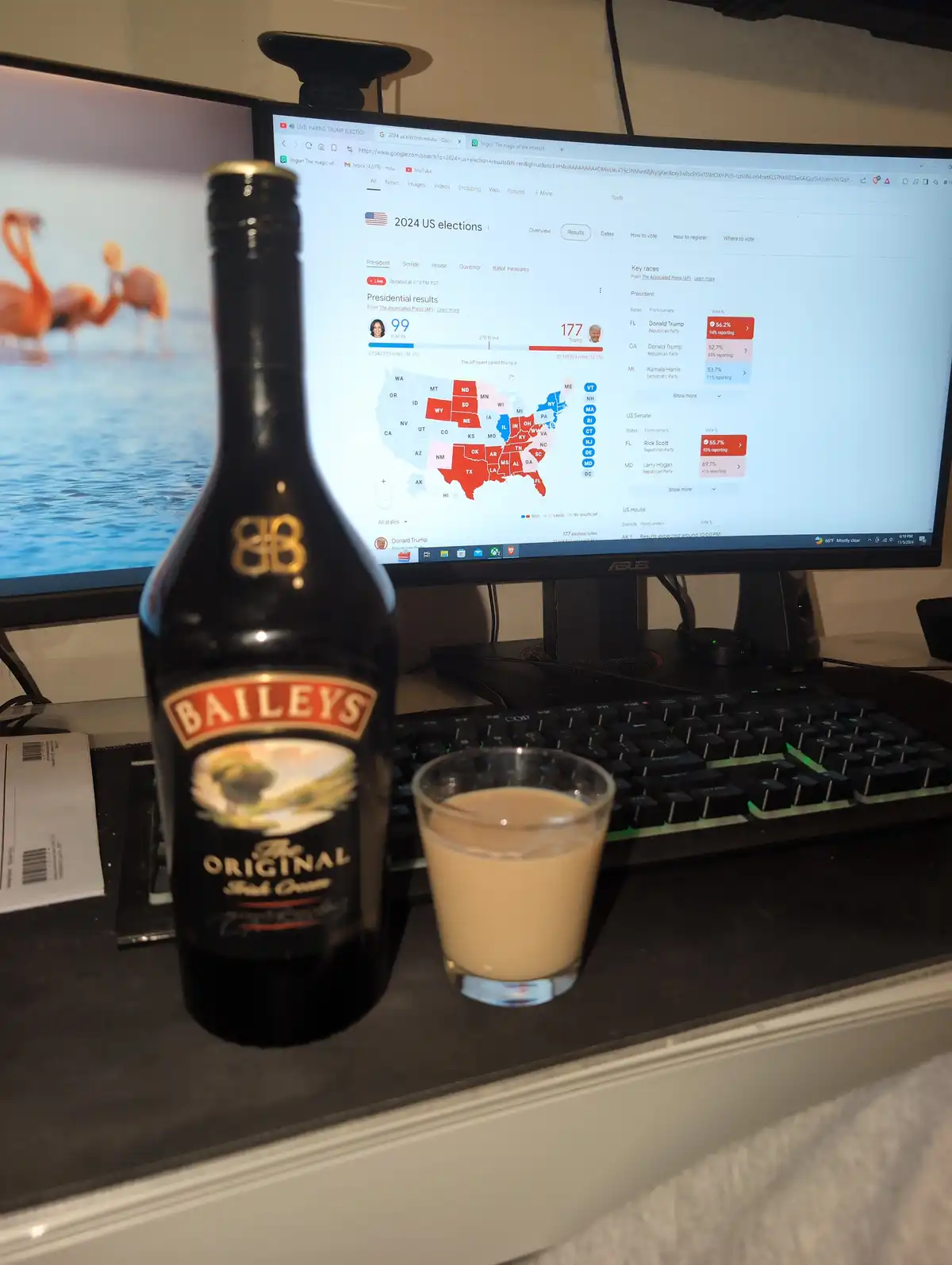 A bottle of Baileys Irish Cream and a glass of the drink sit on a desk in front of a computer monitor displaying a 2024 US…
