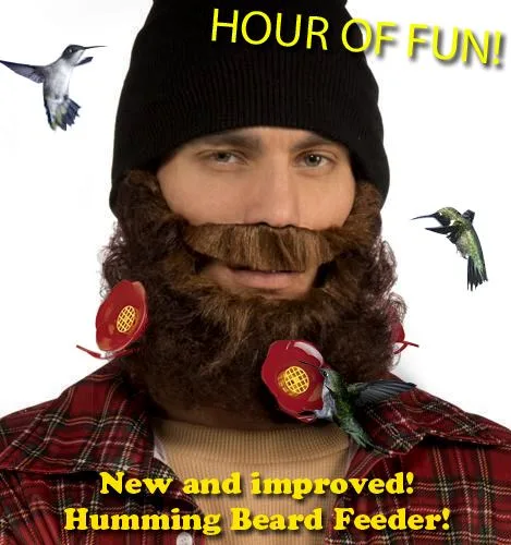 A man wearing a black beanie and a red plaid shirt has a large brown beard with two red flower-shaped feeders attached to…