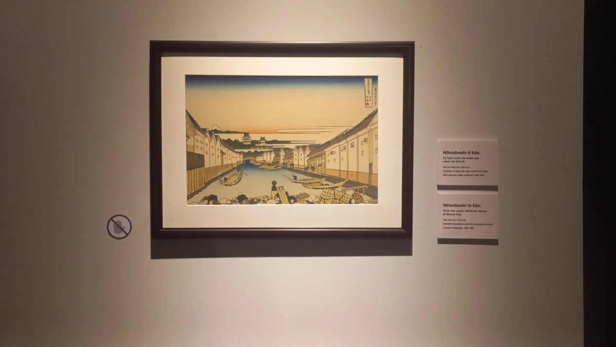 A framed Japanese ukiyo-e woodblock print depicting Nihonbashi in Edo, showing a canal with boats, traditional buildings…