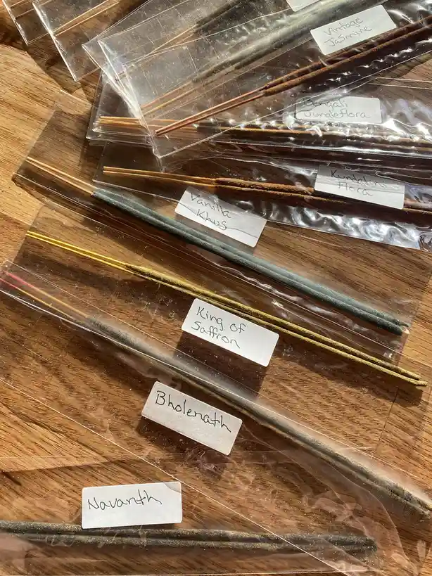 Several packages of incense sticks lie on a wooden surface, each labeled with handwritten names like 'Vintage Jasmine'…