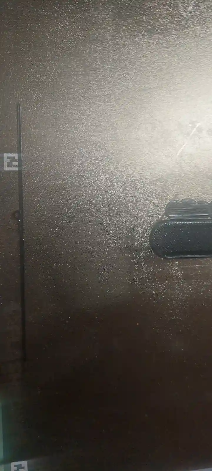 A close-up of a textured, dark brown surface, likely a door or wall, with a vertical black line and a black rectangular…