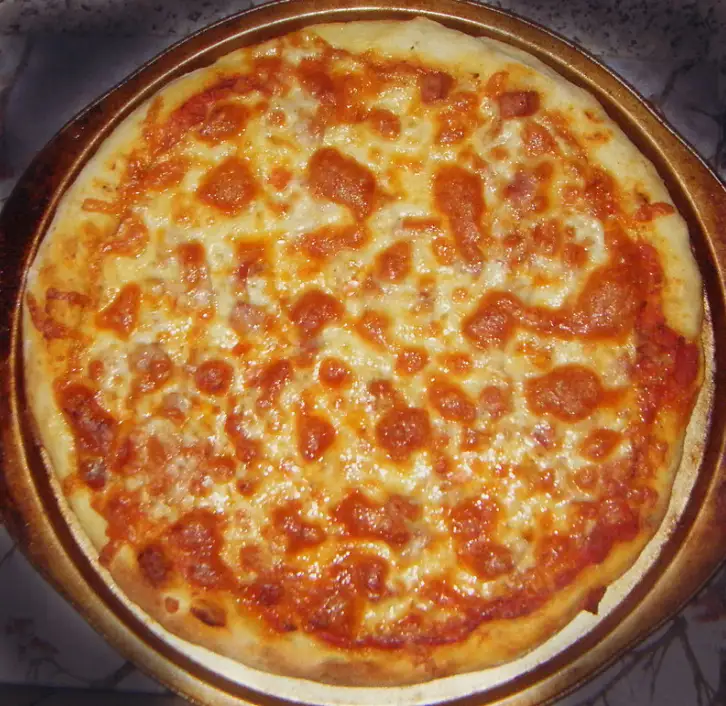 a close-up photo of a pepperoni pizza on a round metal pan, with melted cheese and tomato sauce visible. overlaid text reads…