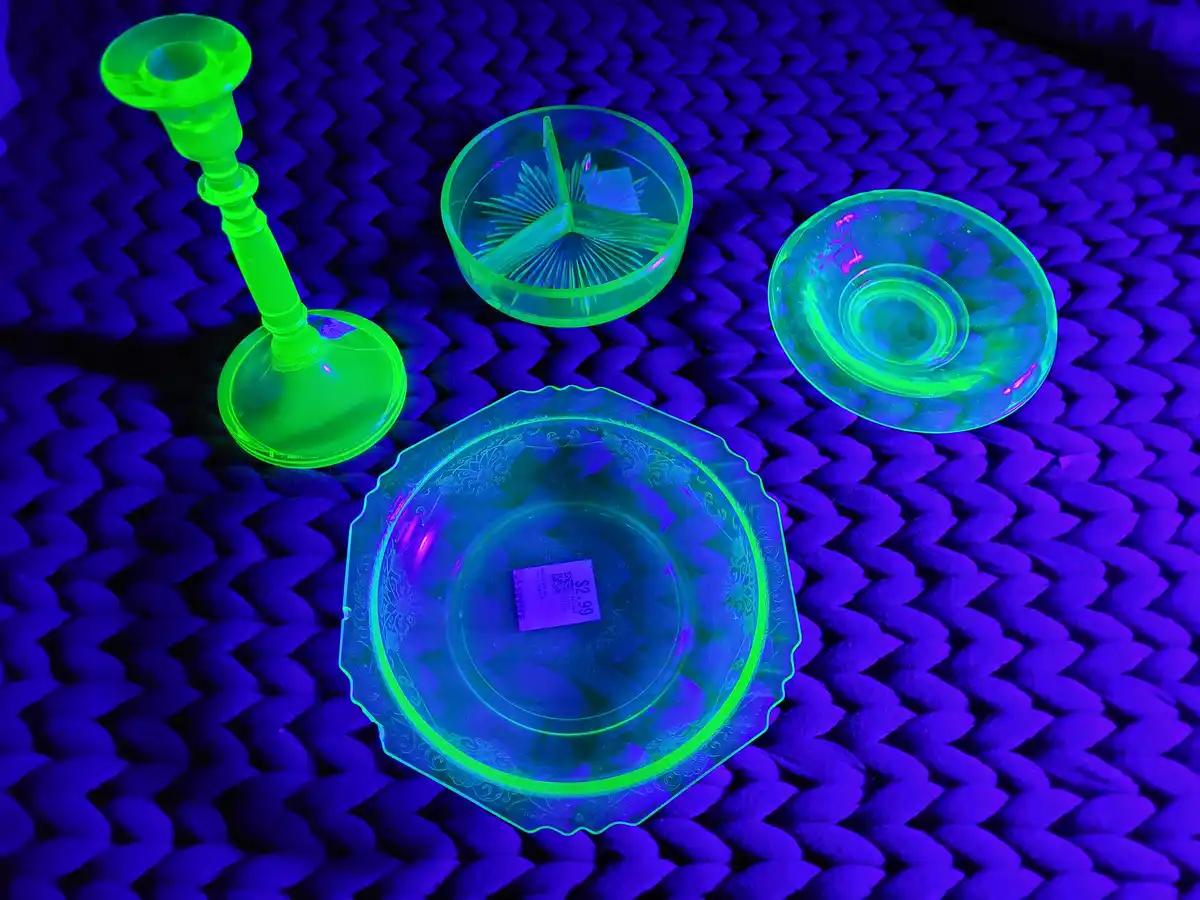 Several vintage glass items, including a candlestick, small bowls, and a decorative plate, glow bright neon green under…