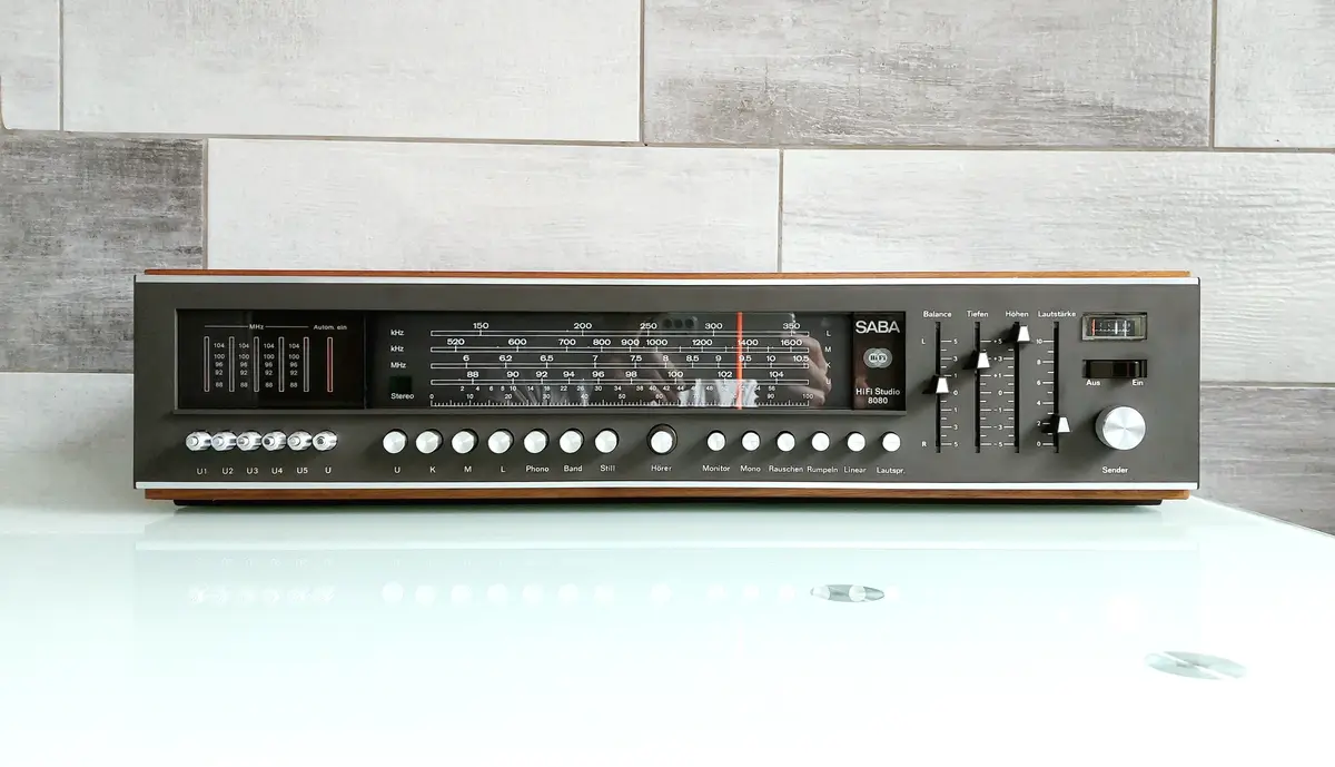 A vintage SABA HiFi Studio 8080 stereo receiver with a wooden casing and numerous knobs and dials, sits on a reflective…