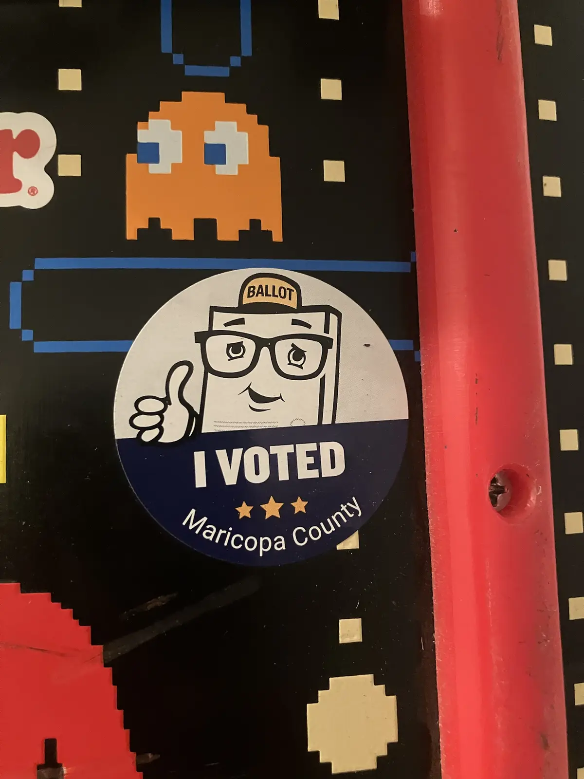 A circular 'I VOTED' sticker from Maricopa County, featuring a cartoon ballot box with glasses and a 'BALLLOT' cap giving a…