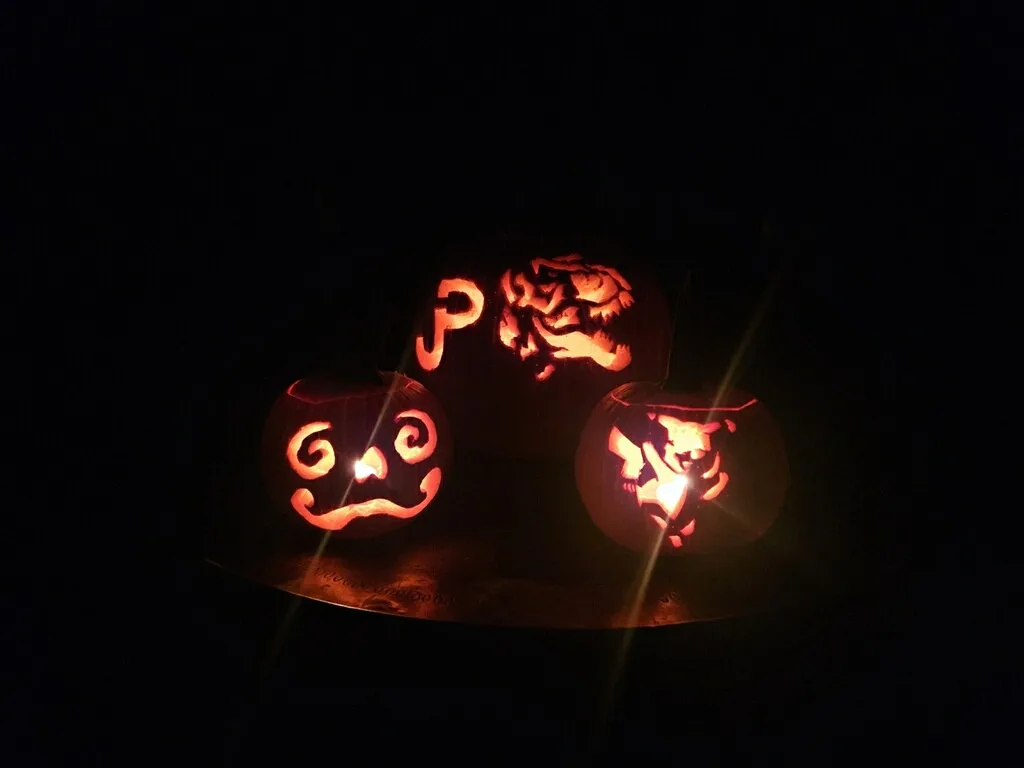 Three illuminated jack-o'-lanterns glow in the dark, carved with a swirling face, a 'P' and a roaring dinosaur, with the…