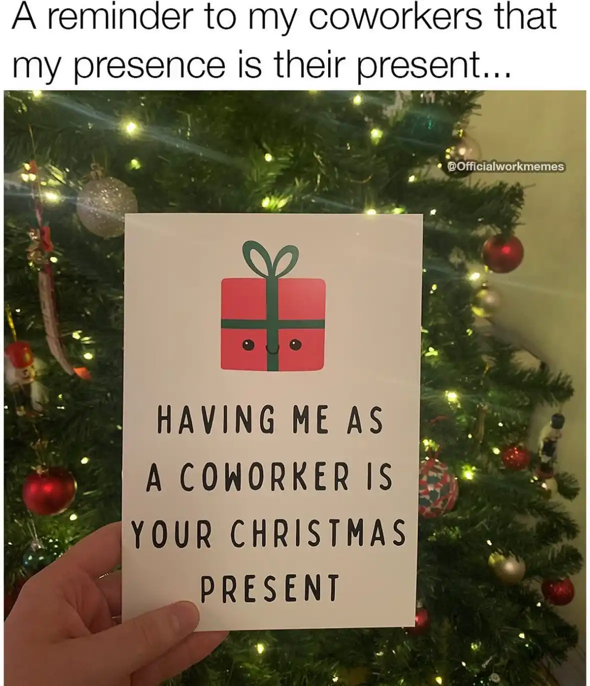 A hand holds a white card in front of a decorated Christmas tree with lights and ornaments. The card features a cartoon red…